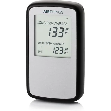 Moniteur Airthings Corentium Home : boîtier blanc allongé tenu à la verticale, son petit écran affichant des chiffres dans la partie supérieure, sur fond clair